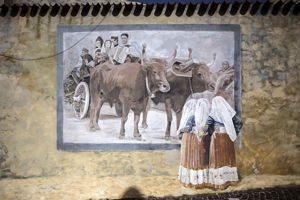 figure femminili in costume tradizionale guardano un murale con carro e figure